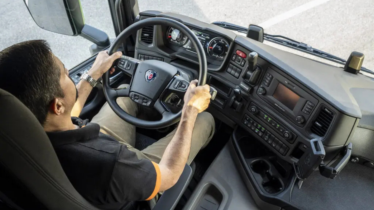 Motorista na cabine do caminhão Scania sentado em banco com suspensão a ar