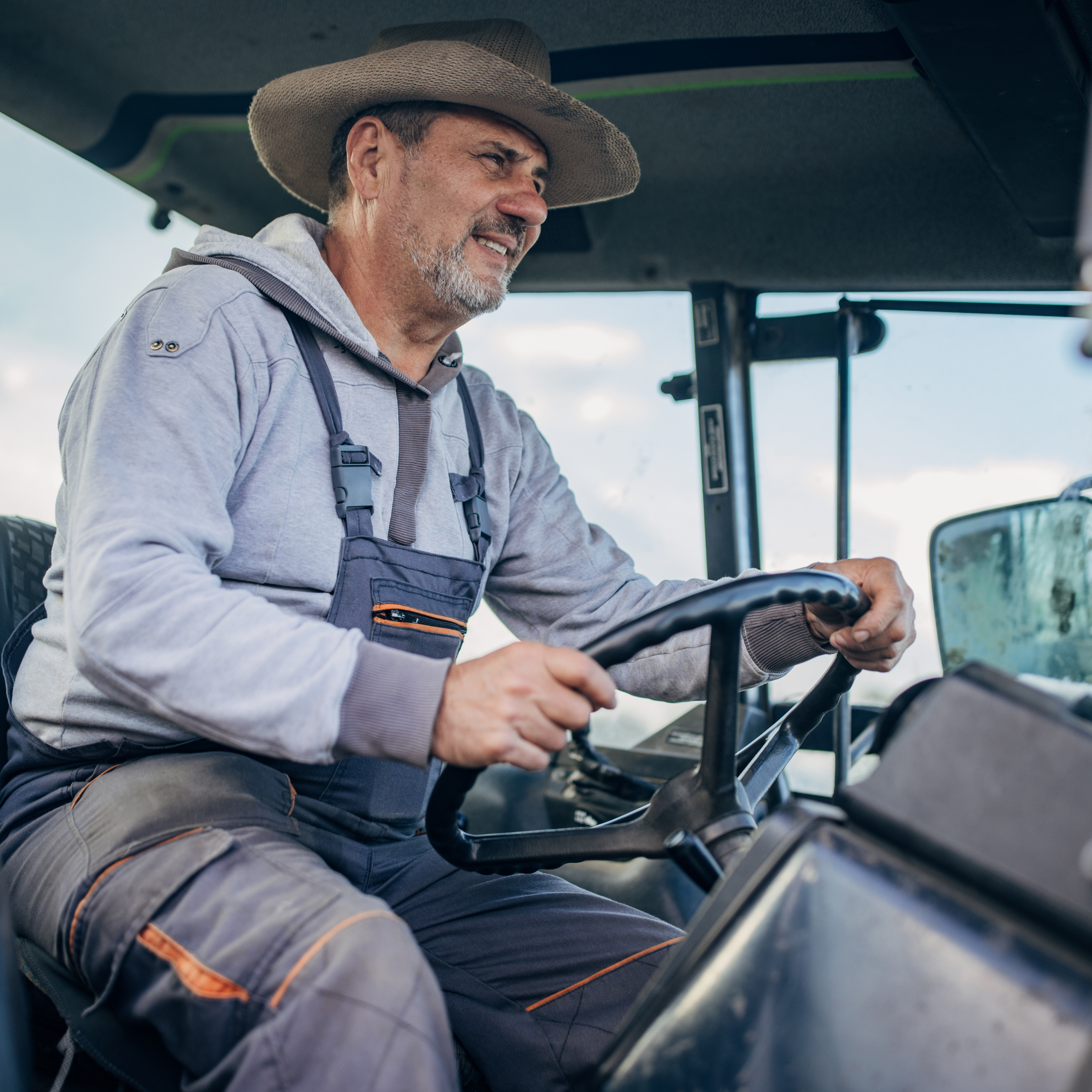 Agricultor operando trator em ambiente de campo, representando conforto e segurança do Banco Eletropneumático 9515.