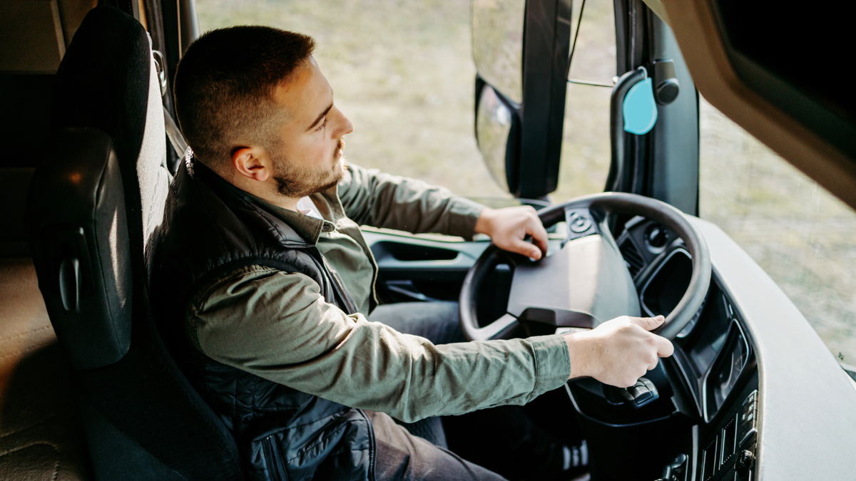 Motorista de caminhão sentado em banco ergonômico com as mãos no volante dentro da cabine